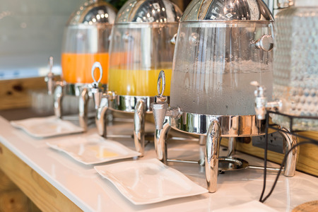 Drinking water, orange and pineapple juice in ice tank at hotel buffet restaurant table. cold drink near variety of foods.の写真素材