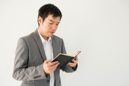 Handsome Asian Businessman read organizer book to check meeting plan for business project. Portrait of working man isolated on white backgroundの写真素材