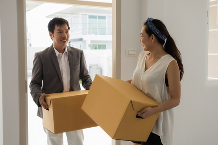 Asian couple carrying cardboard boxes and look at each other at front door. First home with new life and begin. Happy family moving to luxury house.の写真素材