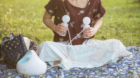 Mother pumping milk to bottles by Automatic breast pump machine in park with foliage sunset bokeh...