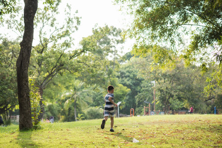 Little Asian boy running up at park meadow with greenery background during sunset in summer. Sport exercise and happiness in field.のeditorial素材