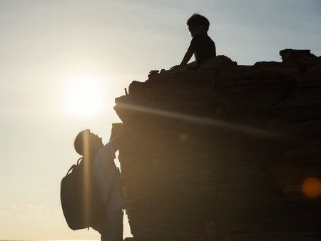 Silhouette hiking woman climbing up to top hill summit to see her son boy during sunset. female mother hike to mountain peak. Family activity concept and outdoor sport.の写真素材