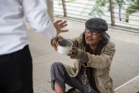 Old handicapped homeless man ask for money while Businessman raise hand to refuse giving money. Poverty and social issue concept. Give and share with sympathy.の写真素材