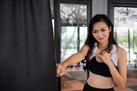 Attractive Asian sporty slim girl with long hair practice Muay Thai boxing by puching at Boxing Sandbag in sport fitness club. Healthy lifestyle for beautiful brunette woman.の写真素材