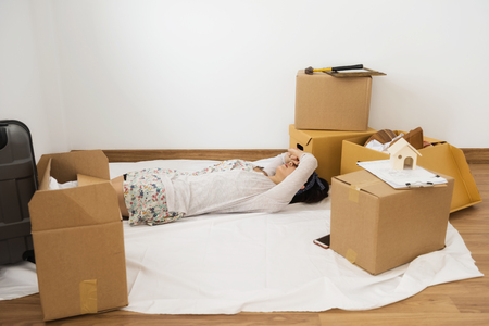 Tired female owner sleep or nap on white fabric sheet of empty room after moving many boxes, luggage and cleaning house. First buying home with new family life to start.の写真素材