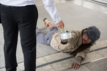 Businessman giving one US dollar bill money to old handicapped beggar or homeless man climbing on...
