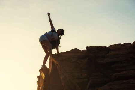Silhouette sporty athlete woman raise hand to sky after hiking to top of mountain summit at sunset with copy space for text. Sport victory, outdoor activity achievement, and healthy concept.の写真素材