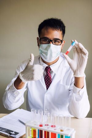 Smiling Arab Lab Technician Thumb Up in Laboratory. Laboratory researcher hold test tube with red chemical liquid. Science and research concept to develop medicine.の写真素材