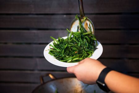 chef scoop hot swamp cabbage or water spinach into dish after cooling on burning pan. Heatlhy food of Thai or Chinese crusine with copy space for text.の写真素材