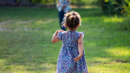 Rear shot of cute girl kid, 2 years old, running on field to reach to her brother with rim light....