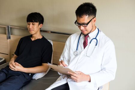 Arab beard psychiatrist doctor fill in medical documents and read lab test result to report to patient on hospital bed. IPD, Inpatient department, or OPD, outpatient for metal sickness guy.の写真素材