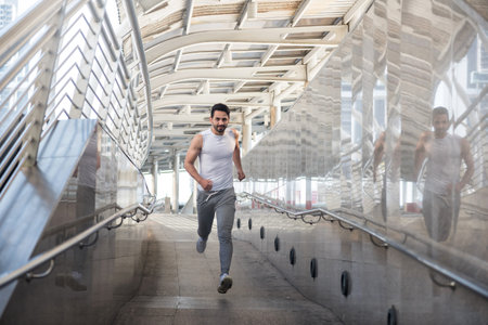 Handsome Italian American happy bearded man in sports clothing running at skywalk bridge in urban...