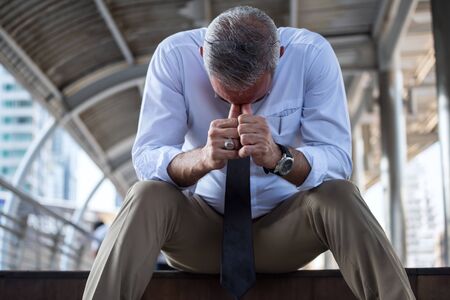 Stressed American old businessman head down and sit on stair in depressed feeling mood after failed in business and being fired. Lay off for 40s to 50s workers. Social issue during Economic recession.の写真素材