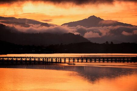 Silhouette view of motion boat and people walking across Mon wooden bridge with twilight sky over Songkalia river at sunrise in Sangkhlaburi, Kanchanaburi, Thailand. Famous travel landmark in Thai.の写真素材