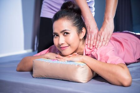 Thai back and shoulder massage to Asian attractive woman by professional female massager in spa salon. Cute happy girl with traditional dress on bed.の写真素材