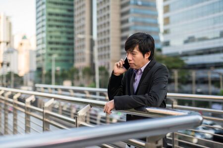 Korean Businessman talking over phone in modern city. Serious entrepreneur, 30s to 40s middle age, man discuss business project by smartphone.の写真素材