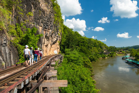 Group of Asian tourist friends walk on World war II historic railway, aka the Death Railway, near river Kwai, Kanchanaburi, Thailand. Famous history travel landmark in Thai.の写真素材