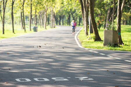 running path of summer park with milestone painted on street with blurred running athlete in morning. Sport and healthy lifestyle.の写真素材