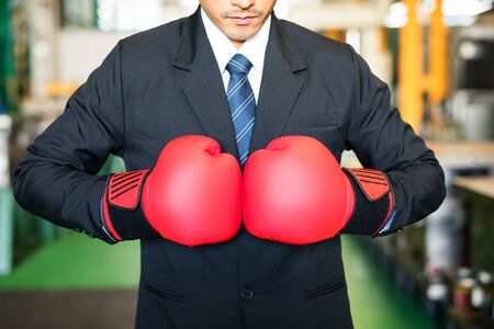 Closeup red boxing gloves on businessman hands ready for corporate battle. Man in suit shirt and tie holding combat gloves together. manufacture factory in bad economy concept.の写真素材