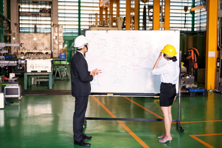 Factory manager discuss with female worker at white board in manufacturing factory. Meeting to set up quality control (QC). Successful industry concept. Selective focus at process flow on board.の写真素材