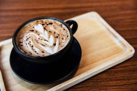 Hot Coffee cup with latte art foam of flower floral pattern on wood table in coffee shop with copy space for text. Drink and relax lifestyle.の写真素材