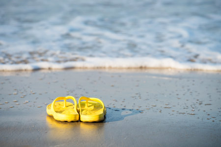 Yelllow flipflop shoes on beach with motion wave in Ao Nang, Krabi, Thailand. sandals on sand for...