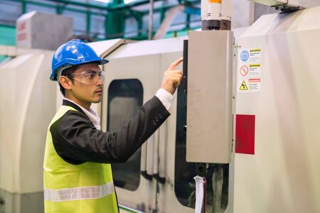 Waist up factory manager with hardhat and protection glasses command automate robot machine on monitor console in factory workshop. Manufacturing industry with technology.の写真素材