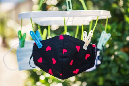 Children fabric face masks with heart paint hang after washing in sunny day with blur foliage light bokeh of green garden background, Reuse to prevent covid or coronavirus pandemic disease. Stay home.の写真素材