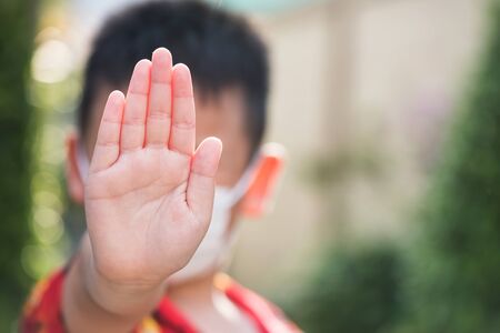 stop hand gesture with white medical mask to prevent covid-19 or coronavirus pandemic disease. New normal, stay home, social distancing for children with sunset bokeh background.の写真素材