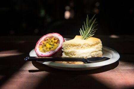 cheesecake with  passion fruit sauce on wooden table with light shade at coffee shop cafe. Yellow sweet dessert with dark background.の写真素材