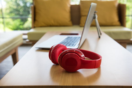 Red leather headphones and silver computer laptop on wooden table. Music and gadget technology...