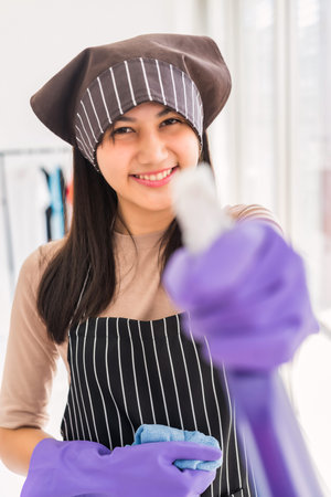 Beautiful Asian smiling girl with gloves hold rag and bottle spray for cleansing home. Cleaning...