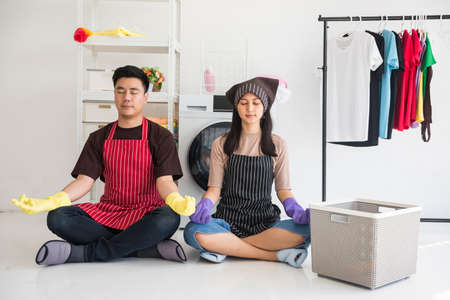 Young Asian husband and wife couple with apron dress together perform yoga during waiting laundry machine to washing. housework and housecleaning in weekend.の写真素材