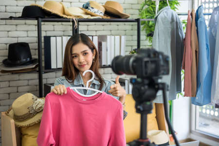 Live streaming content for selling fashion online by digital camera on tripod. Beauty blogger or internet influencer. young Asian woman vlogger blogging show pink shirt on social media.の写真素材