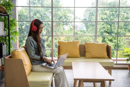 Smiling beautiful Asian businesswoman wearing jacket shirt relaxing using laptop and headphone....
