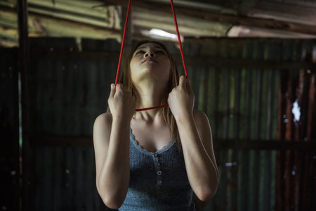 frightened Asian woman look at gallows and hold red rope noose to commit suicide in abandon house....