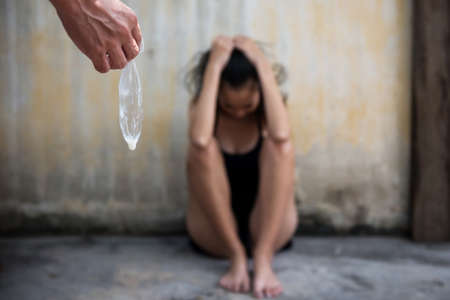Closeup hand hold used condom with white semen or sperm. stressed sad woman victim sit near wall after being raped. Stop Sexual harassment or rape concept.の写真素材