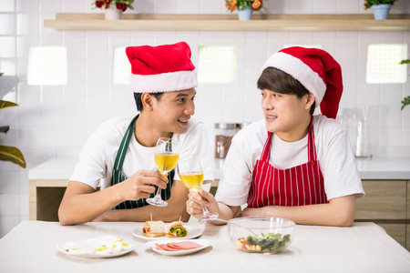 LGBT Asian gay couple with santa hat and apron toast wine and eat salad and sandwich at lunch to celebrate Christmas and 2021 new year after cooking food. Happy together. Same sex family.の写真素材