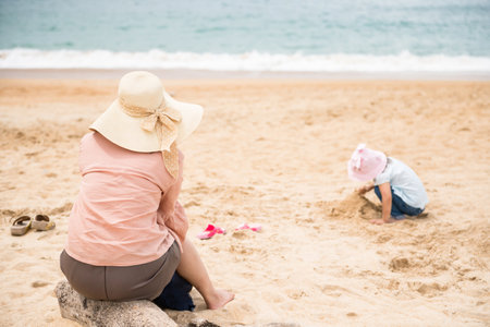 Asian mother with hat look at her daughter to make sand castle on the beach in Phuket, Thailand. Family holiday vacation trip in summer.の写真素材