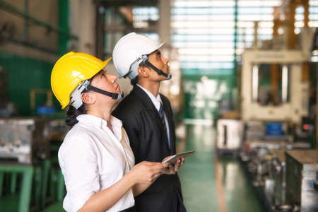 Factory auditor and inspector manager look up to check factory hardware safety for quality control. Young worker hold tablet to use corporate application to submit examine report.の写真素材