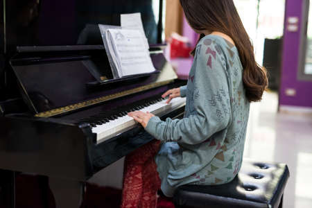 Rear of Asian woman pianist playing on classic Piano keyboard. Closeup fingers to music instruments. leisure and hoppy in house concept. mental therapy by song.の写真素材