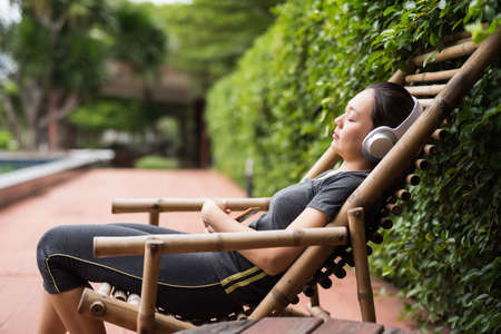 Fitness Asian young woman sleep and listen online music by wireless earphone after running exercise in morning. Rest and relax from exhausted or tired.の写真素材