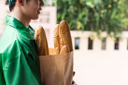 deliveryman hold baguette bread in bakery paper bag and wait for customer to pick up. New normal of delivering business for famous of online e-commerce due to covid-19 changing customer behavior.の写真素材