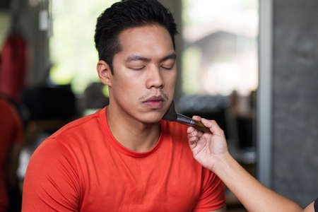 Behind the scene. Make up to Muscle Asian fitness young man to photo shoot in gym.  makeup artist applying cosmetics to sport guy.の写真素材