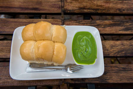 Fresh stream loaf bread with green pandanus leaf egg custard in white dish on wooden table. Thai style dessert or sweet. Unhealthy eating lifestyle.の写真素材