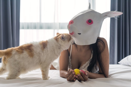 Sexy Asian woman in cute bunny mask and sexy white pajama hold colorful eggs and play with exotic...