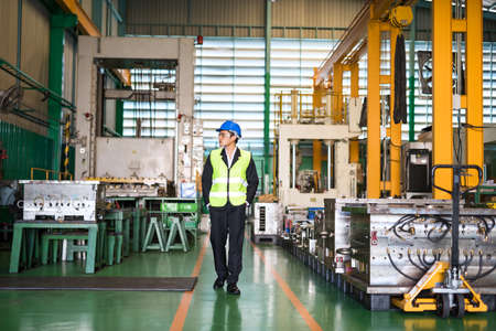 Waist up Asian businessman or young inspector with hardhat walk along production department to examine machines in manufacturing factory. Safety first for heavy industry.の写真素材