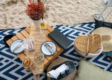 Wicker basket with tasty food and champagne drink for romantic picnic on white sand beach. Beautiful...