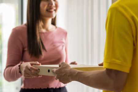 Closeup delivery courier hands deliver pizza food to smiling business woman at meeting room door inside office building. New normal to order food by mobile application during  virus pandemic.の写真素材