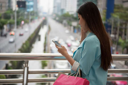 Beautiful Asian foreign tourist woman find shopping location by GPS navigator from smartphone in Bangkok modern city at winter. 4G Technology to travel around the world.の写真素材